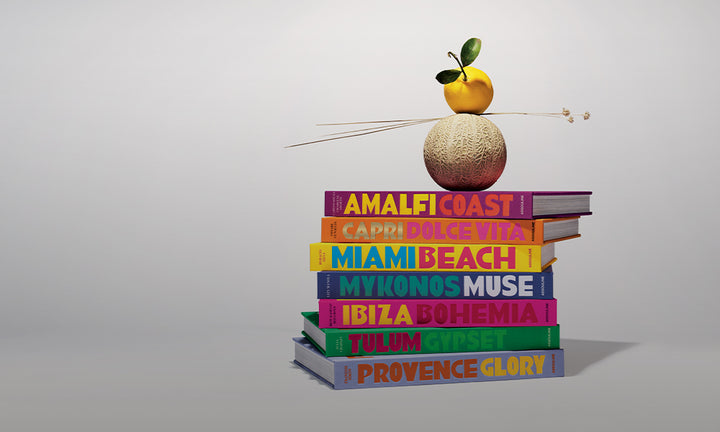 Stack of colorful books laying against a white background with a cantaloupe and a lemon